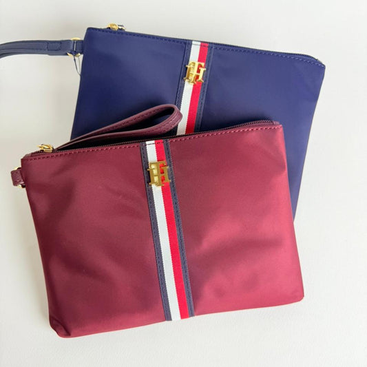 Two Tommy Hilfiger bags — one blue and one red — featuring gold zippers and signature red, white, and blue stripes.